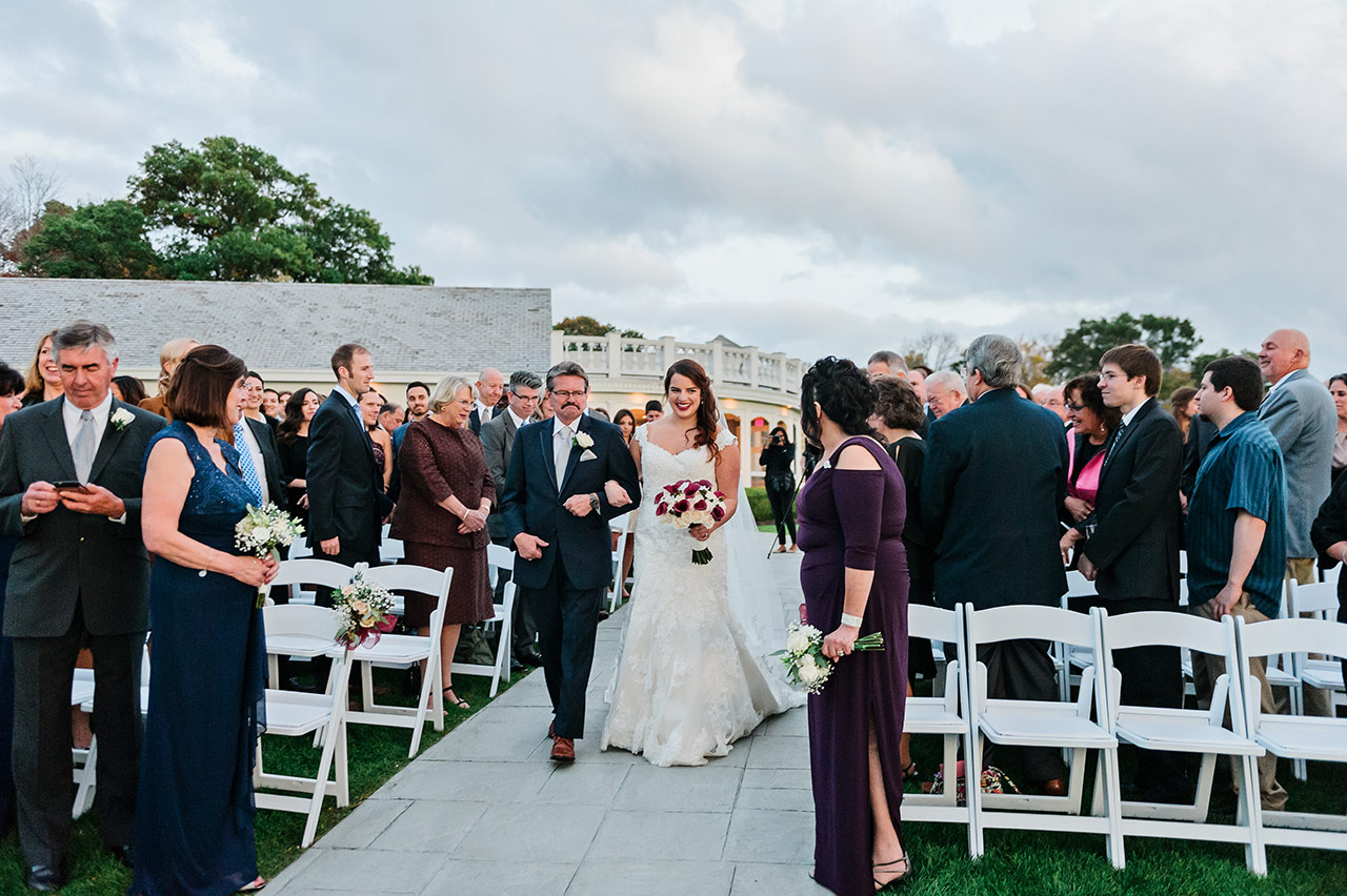 Bride walks down the aisle during an outdoor lakeside wedding ceremony at Candlewood Inn.