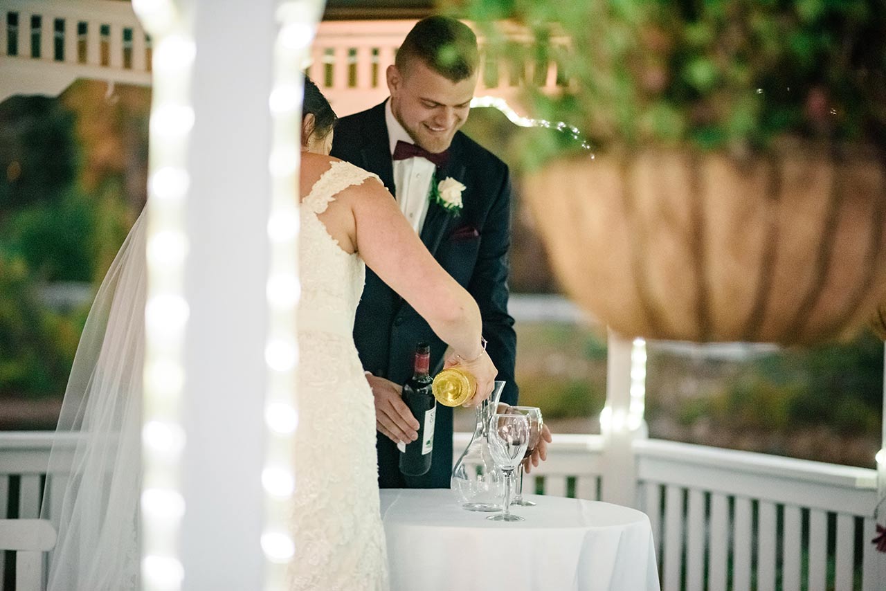 Bride and groom pour wine at an intimate wedding reception table under soft evening lights.