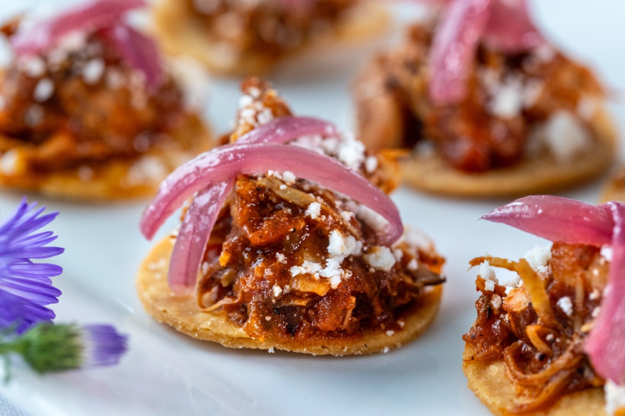 Chicken carnitas bites topped with pickled onions and cheese on crisp tortilla rounds.