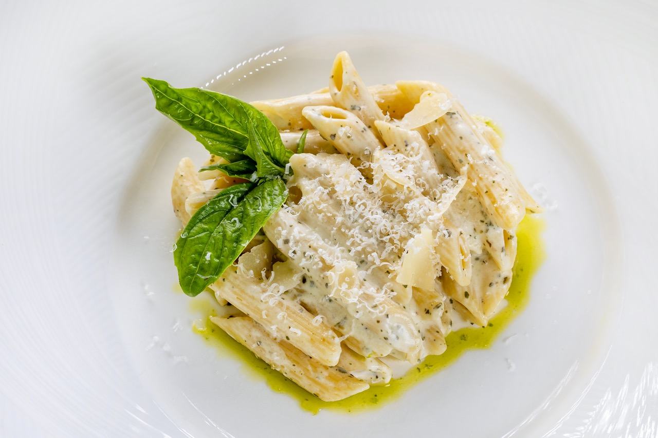 Creamy pesto penne pasta topped with Parmesan shavings and fresh basil garnish.