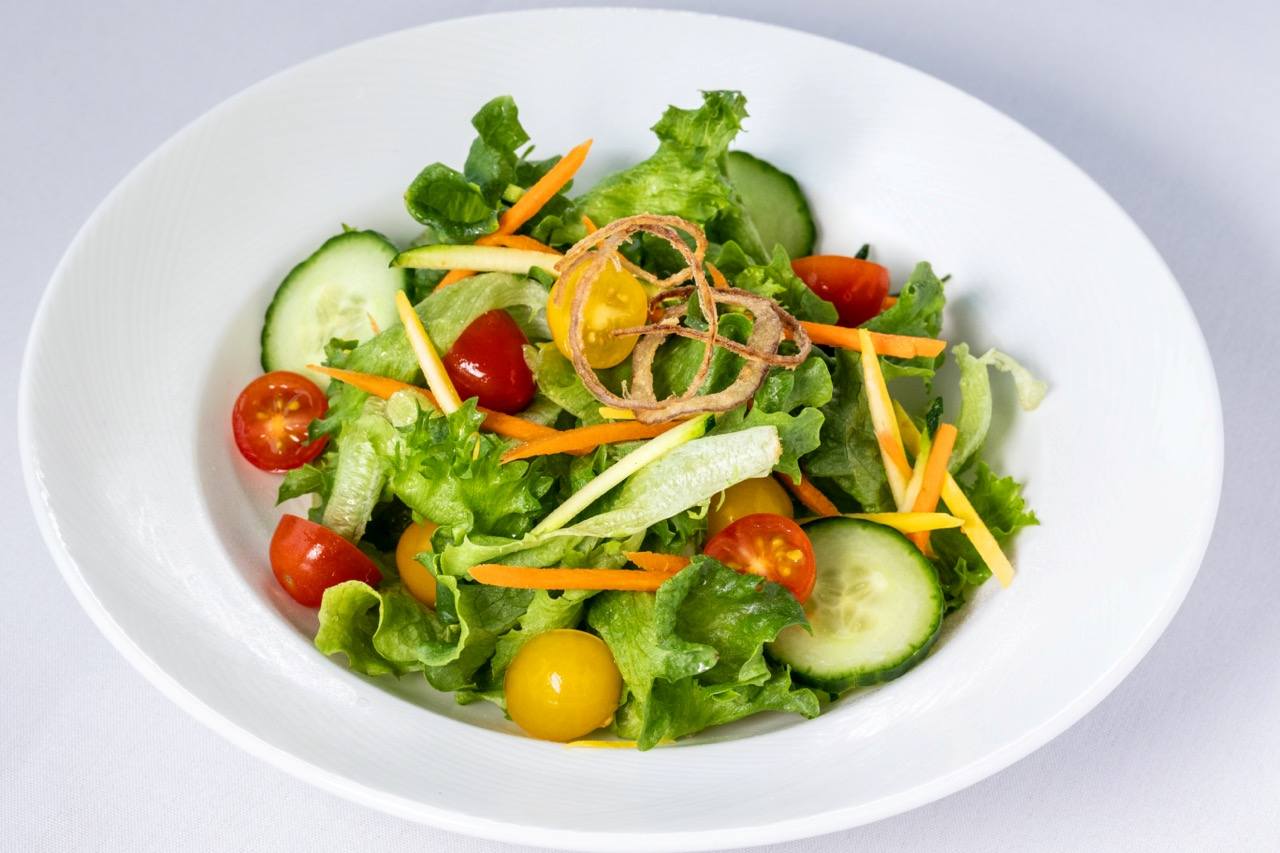 Fresh house salad with mixed greens, cucumbers, tomatoes, carrots, and crispy onion rings.