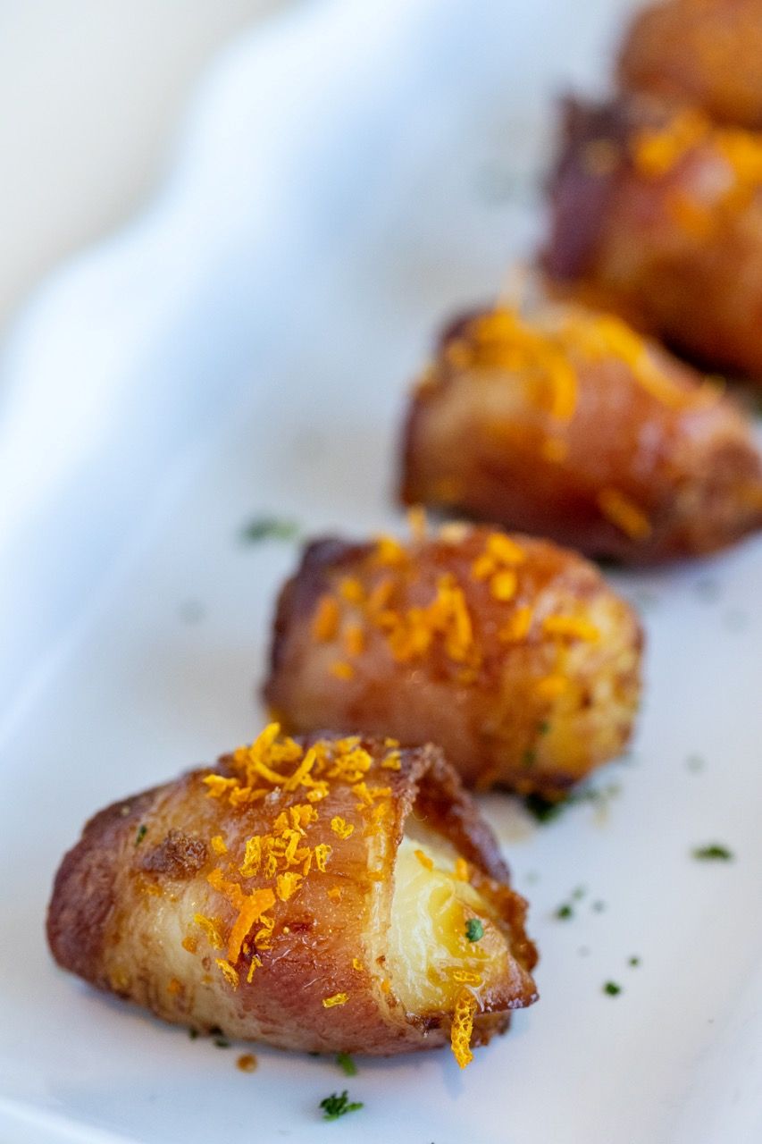 Bacon-wrapped scallops topped with citrus zest, served as an elegant appetizer.