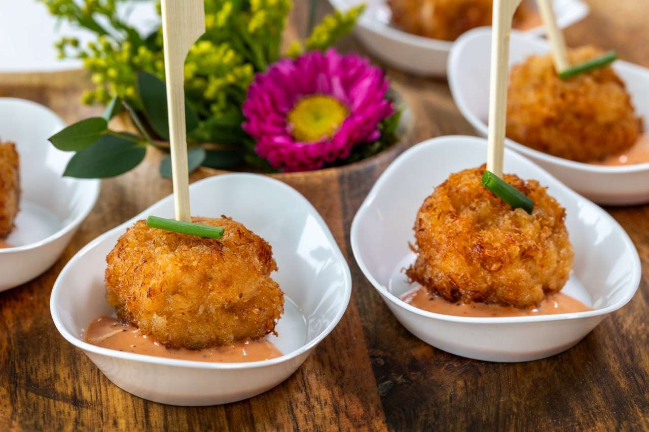 Golden crab cake appetizer served with creamy sauce in individual tasting bowls.