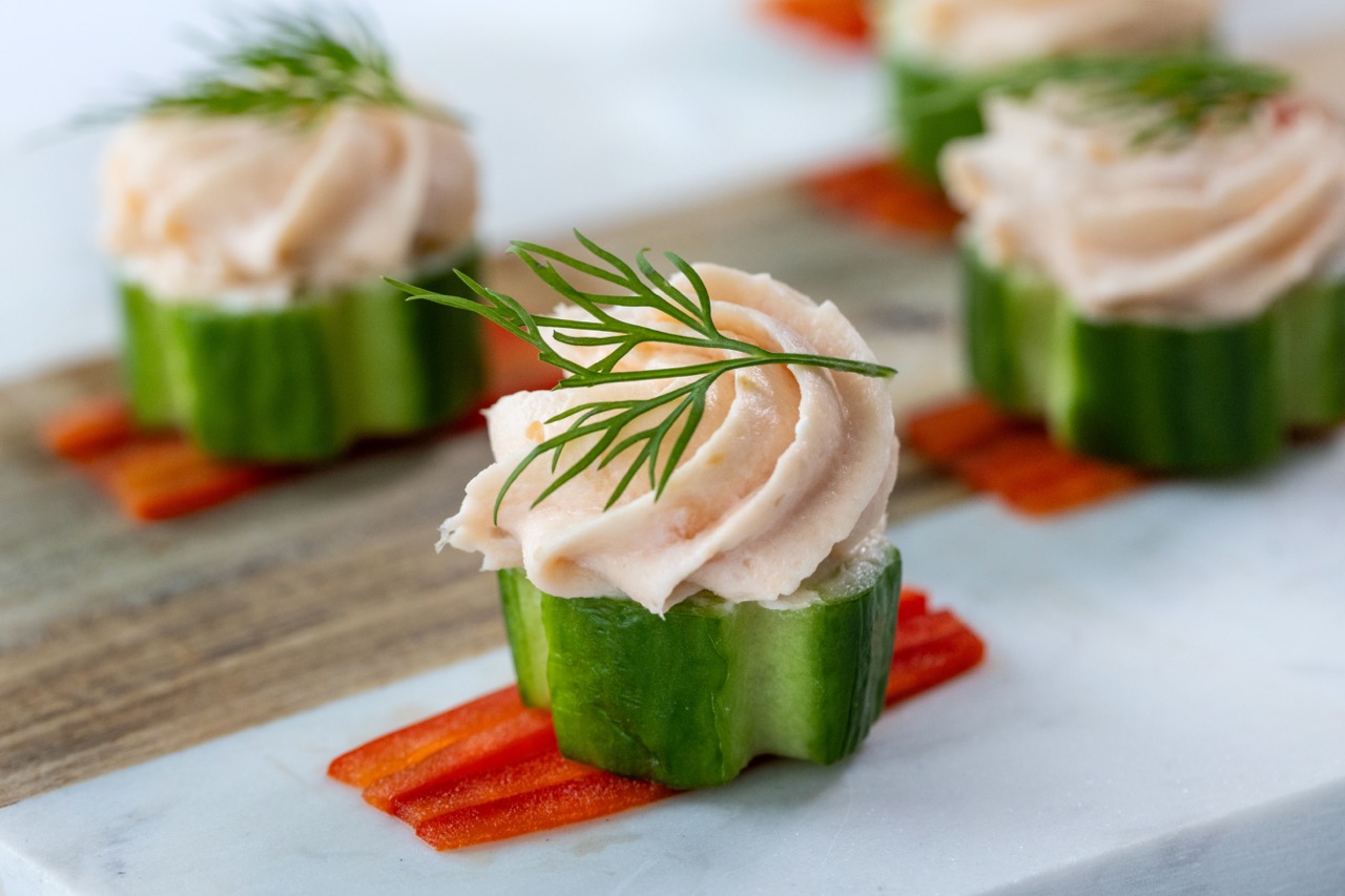 Smoked salmon mousse piped onto cucumber bites, garnished with fresh dill and red pepper.