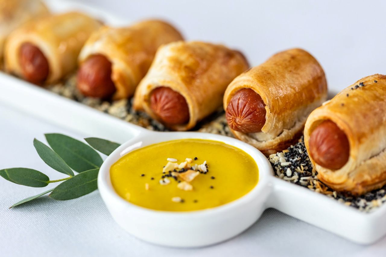 Franks in a blanket served with mustard dipping sauce and everything seasoning garnish.