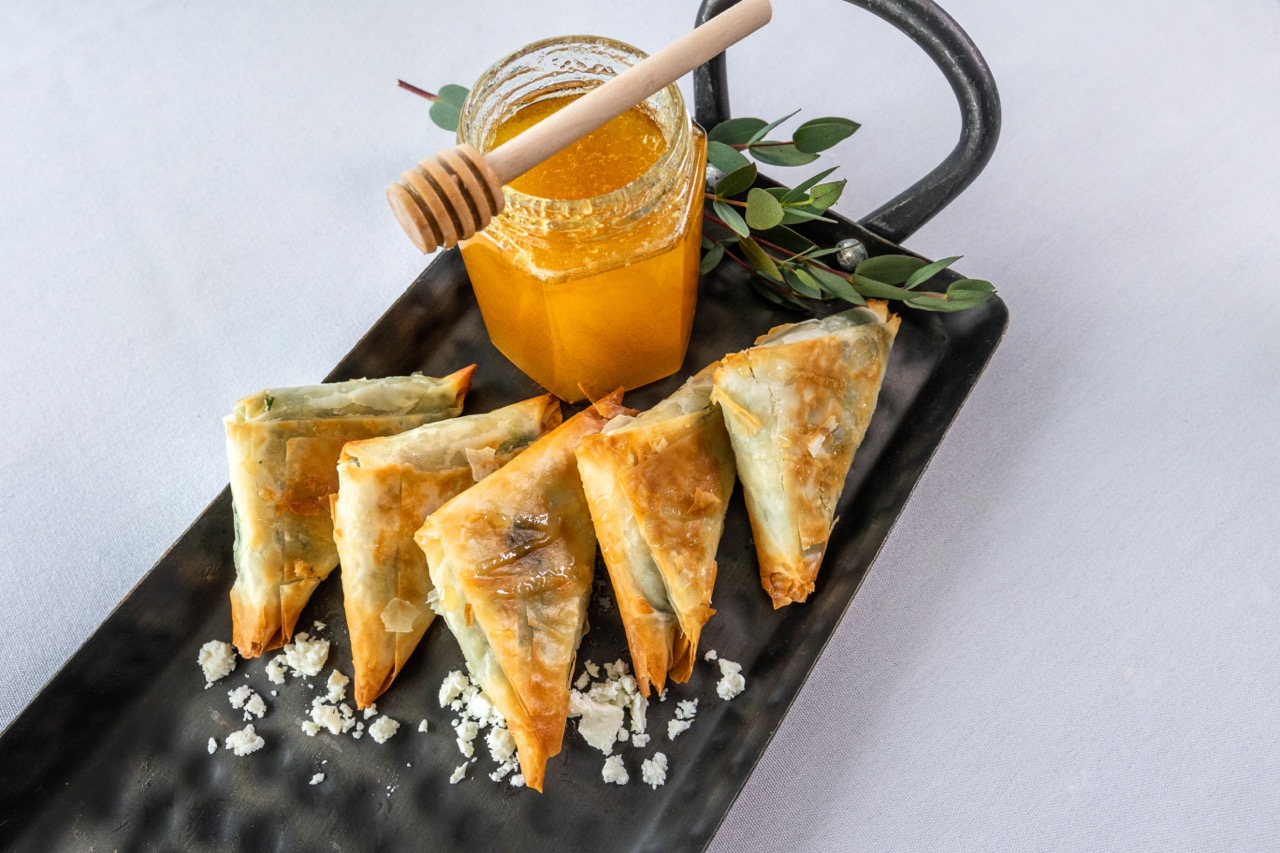 Spanakopita triangles with flaky pastry, spinach filling, feta crumbles, and honey drizzle.