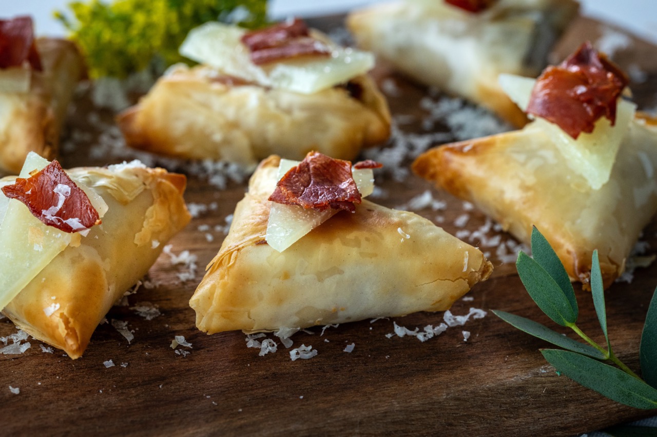 Manchego Cheese Bite with crispy pastry, aged cheese, and cured meat garnish.
