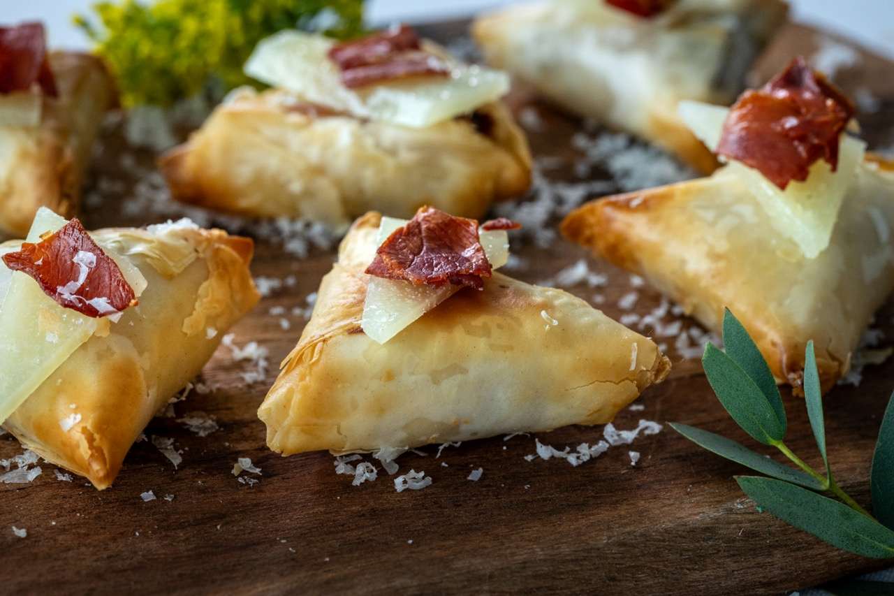 Manchego Cheese Bite with crispy pastry, aged cheese, and cured meat garnish.