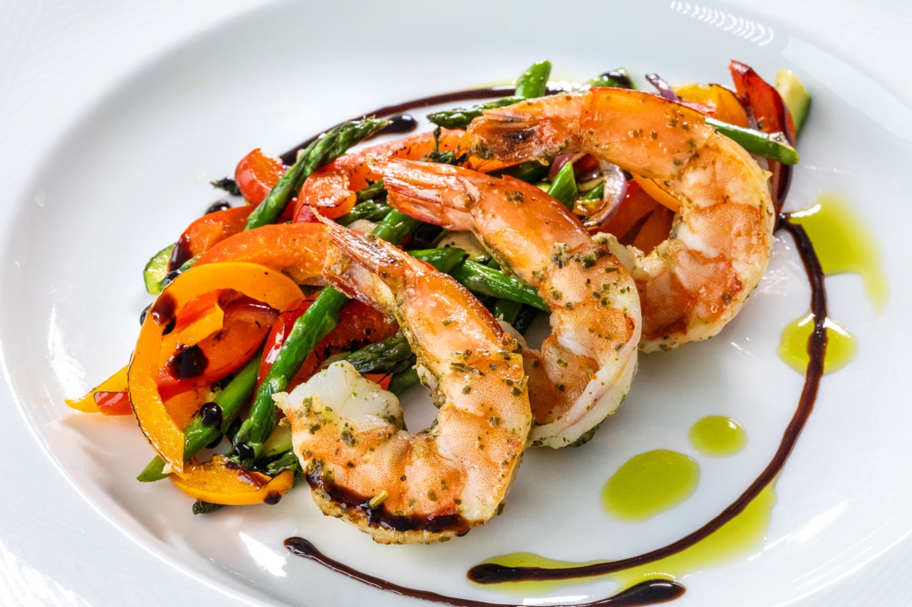 Mediterranean shrimp served with colorful vegetables, balsamic glaze, and herb oil drizzle.