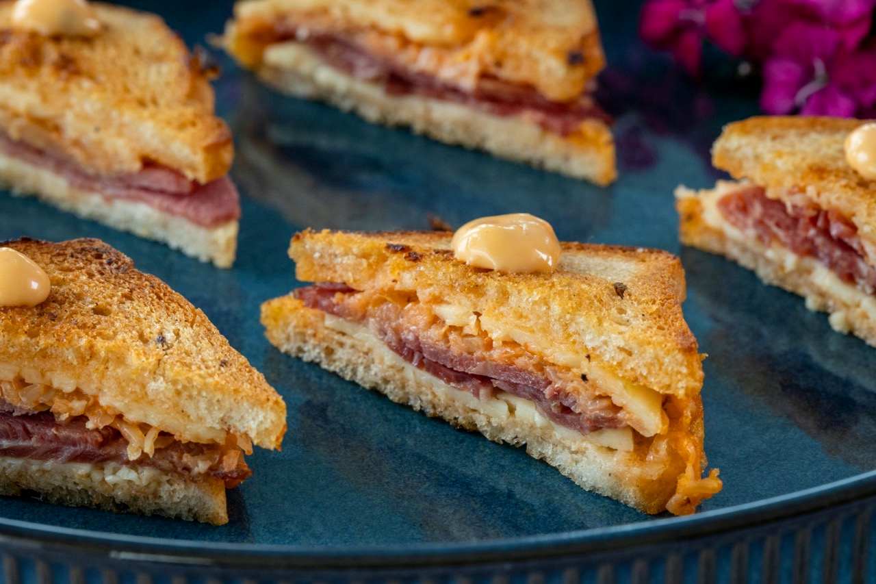 Mini Reuben sandwiches with corned beef, melted cheese, and creamy dressing on toasted bread.