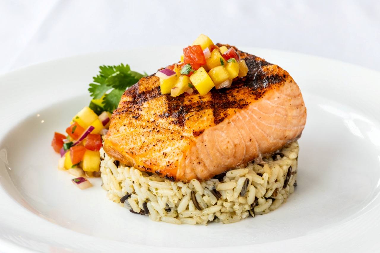 Grilled salmon fillet served over wild rice with fresh mango salsa and cilantro garnish.