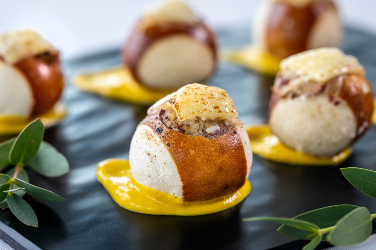 Pastrami Pretzel Bite topped with melted cheese and served on a mustard sauce.