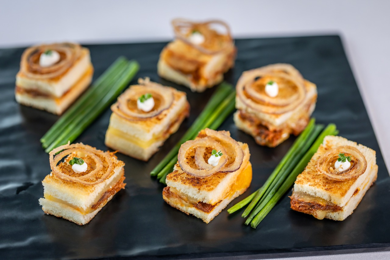 Brisket grilled cheese bites topped with crispy onions and served as savory appetizers.