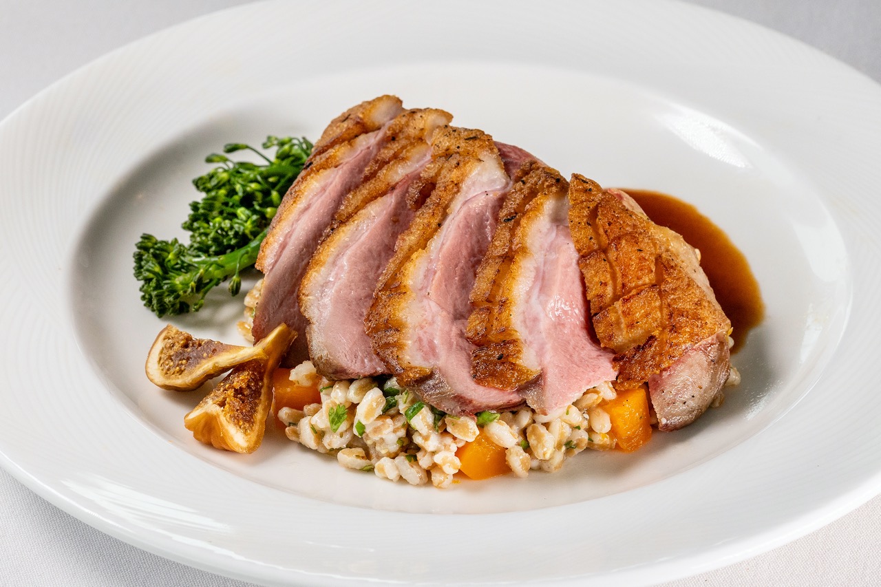 Seared duck breast with crispy skin, grains, figs, and seasonal vegetables in a savory glaze.