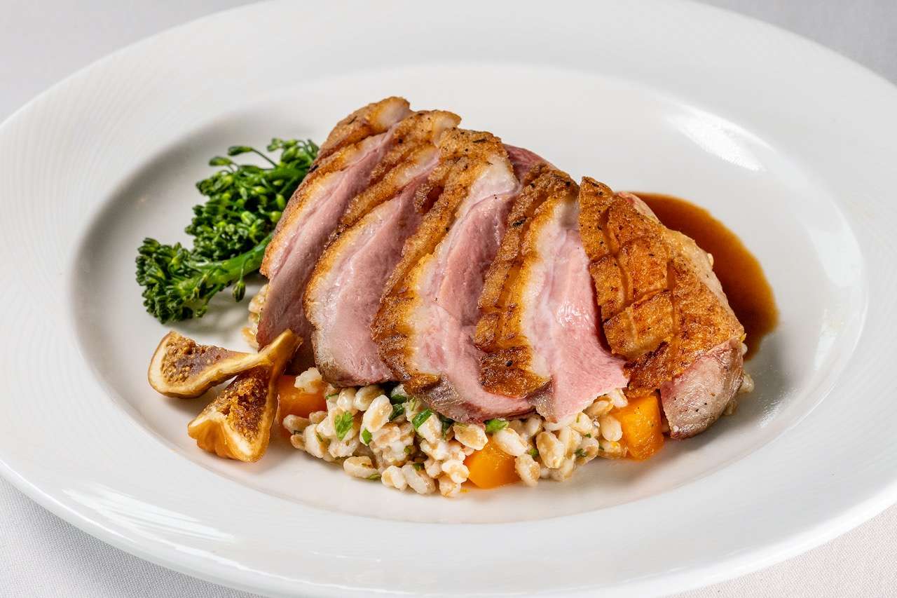 Seared duck breast with crispy skin, grains, figs, and seasonal vegetables in a savory glaze.