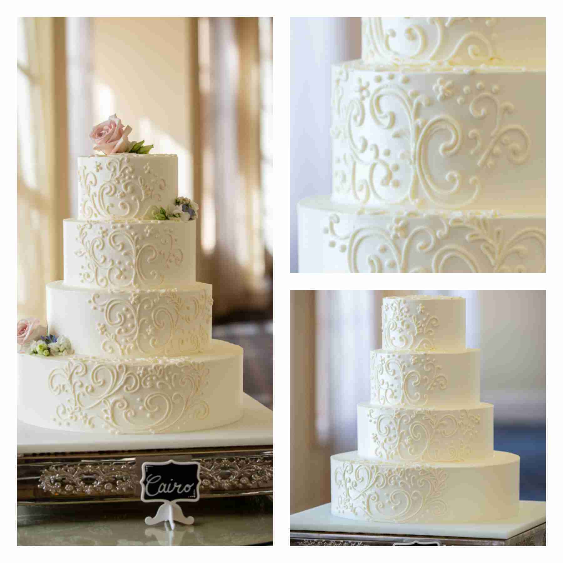 Four-tier white wedding cake featuring elegant piping detail and light pink floral accents.