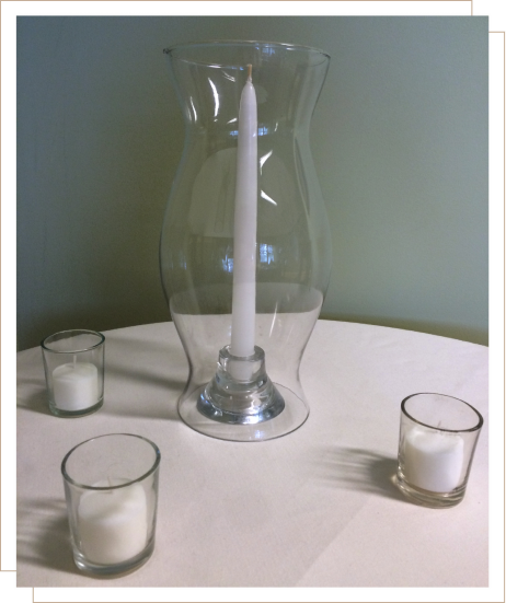 Glass hurricane vase with a taper candle surrounded by three smaller votive candles.