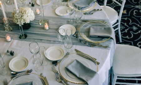 Elegant wedding table setting with white and grey linens, glass chargers, and candles.