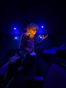 Performer in costume with glowing accessories at SpookyFest 2026, Hollywood's horror arts festival, under dark blue lighting.