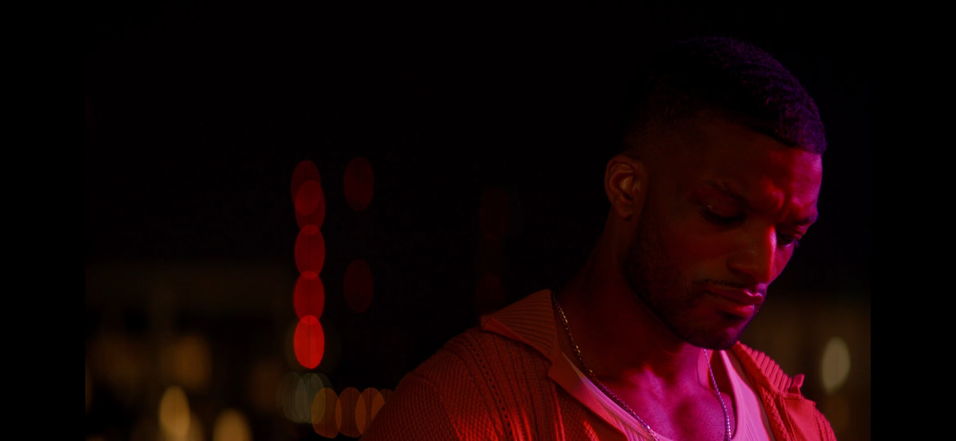 A young man with a serious expression, illuminated by red and purple lighting, appears to be in deep thought or concentration during a nighttime event.