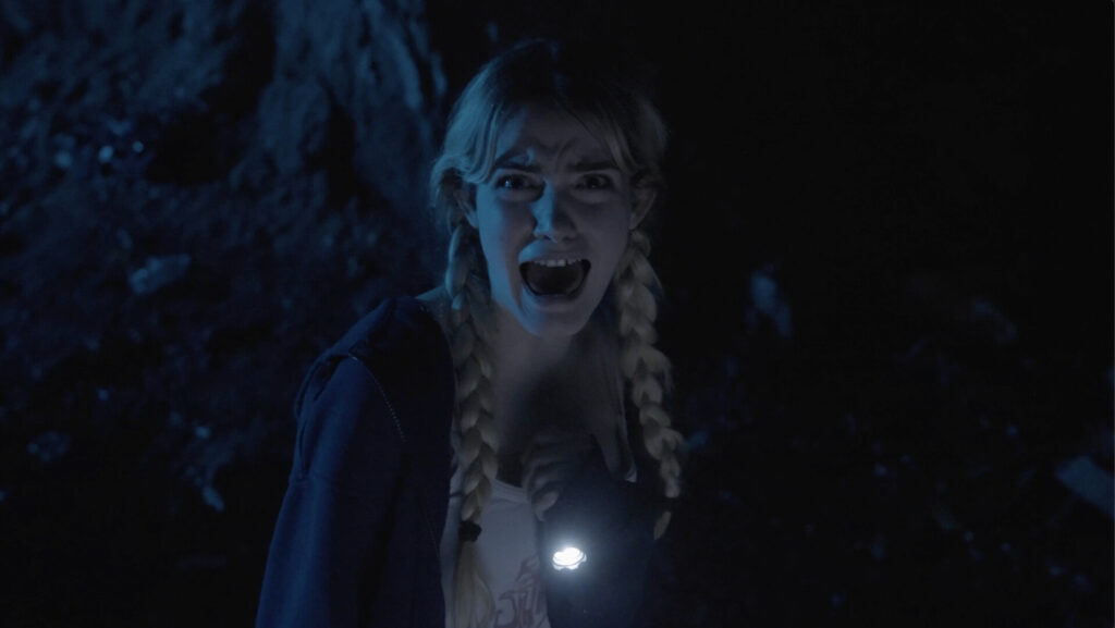 A young woman with braided hair and a flashlight in a dark, eerie setting, screaming with fear.