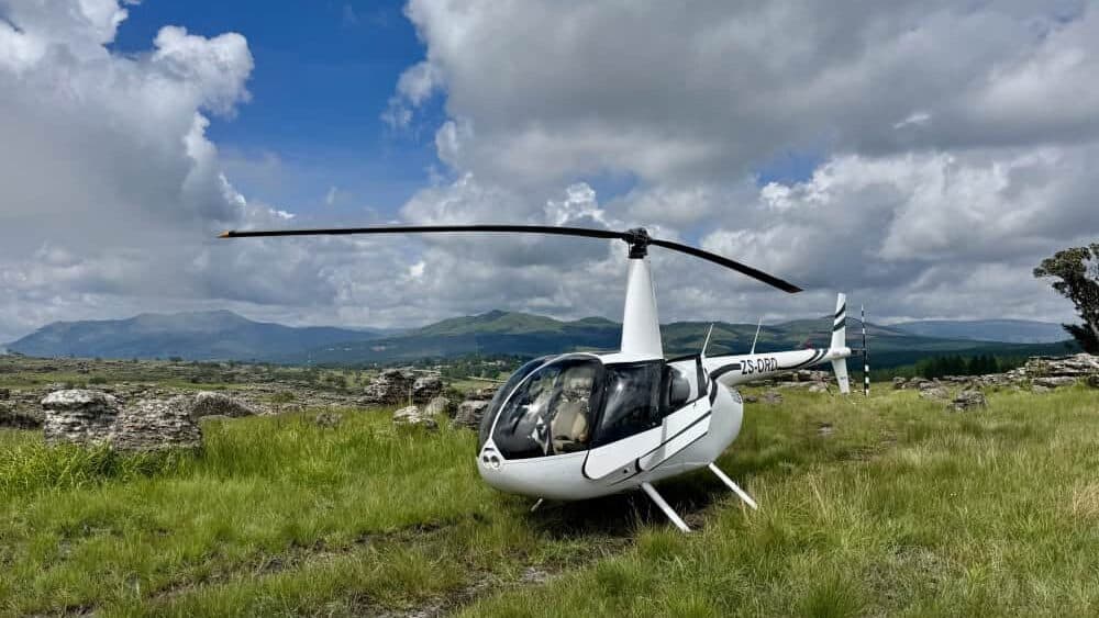 Aerial helicopter tour over lush green landscape with rolling hills and cloudy sky in South Africa.