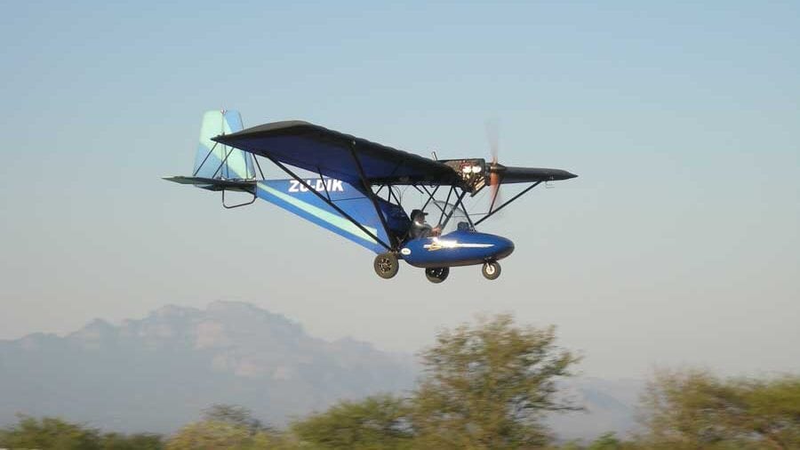 Aerial view of a blue ultralight aircraft flying over the South African landscape, showcasing adventure tourism and scenic flight experiences.