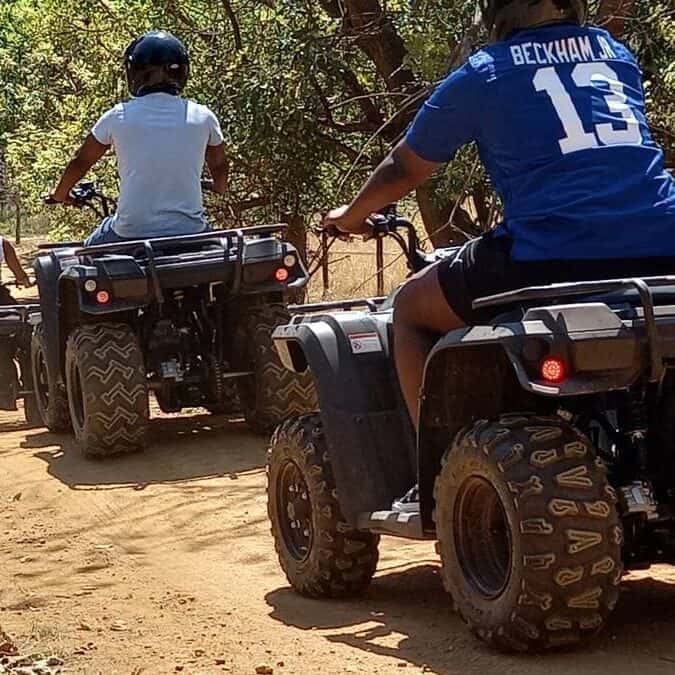 ATV riding adventure in a natural outdoor setting with two riders on quad bikes, surrounded by trees and dirt trail.