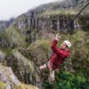 Climber enjoying a thrilling zip line adventure over lush green mountains in South Africa, surrounded by misty weather and rugged cliffs.