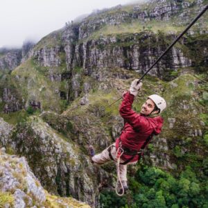 Climber enjoying a thrilling zip line adventure over lush green mountains in South Africa, surrounded by misty weather and rugged cliffs.