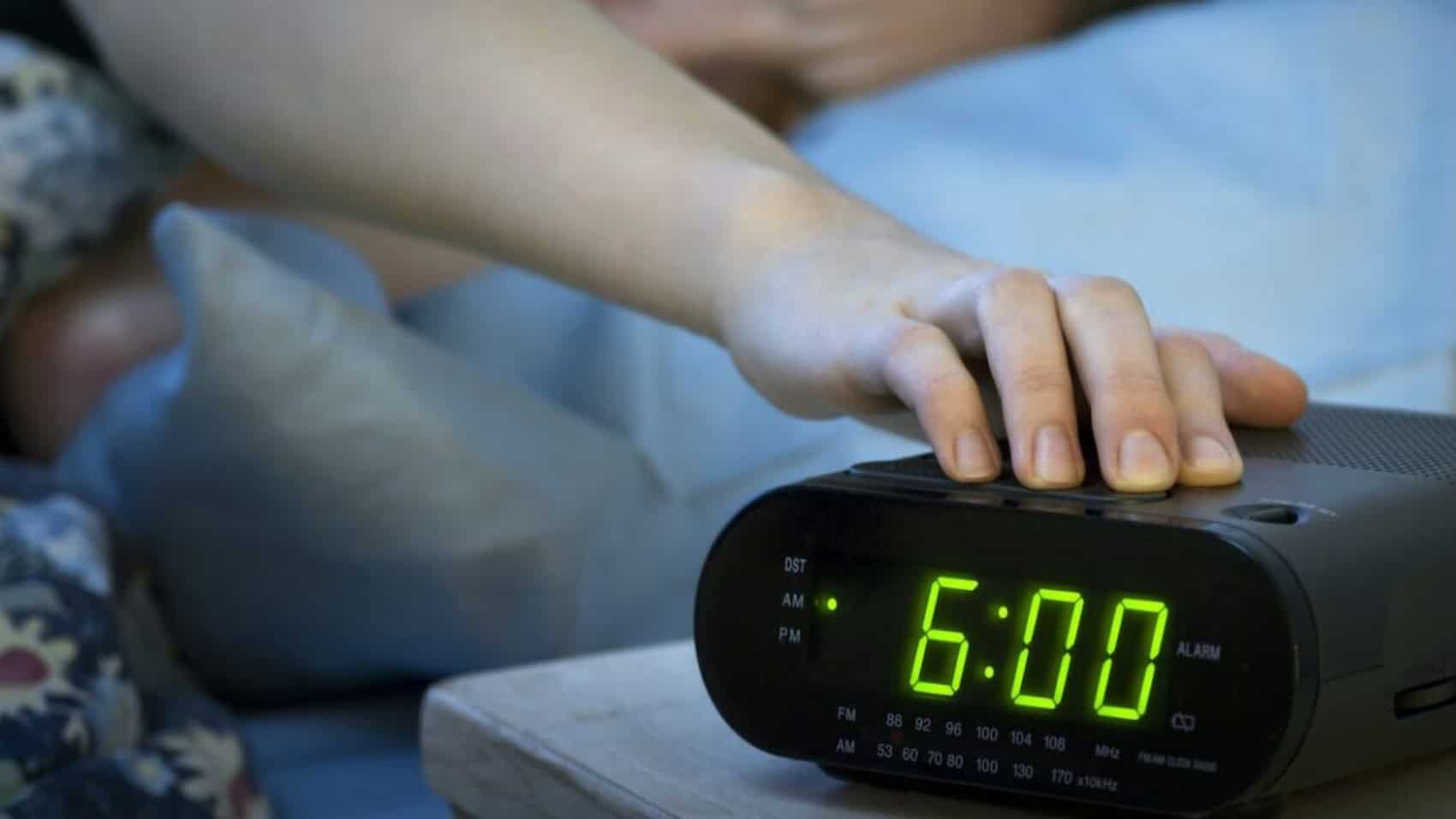 Young woman pressing snooze button on early morning digital alarm clock radio