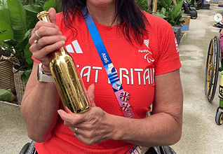 Gold medalist woman holding trophy, outdoor celebration, winter sports, athletic woman with medals, victory, sports achievement, smiling athlete in red shirt.