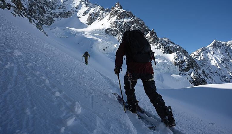 Deep snow mountain climbing in winter, two climbers ascending snowy slopes under clear blue sky, showing adventure, winter sports, and mountain exploration.