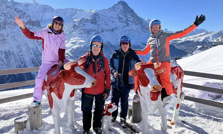 Colourful group of skiers with mountain scenery and carved cow statues on a snowy balcony at a ski resort in the Alps.