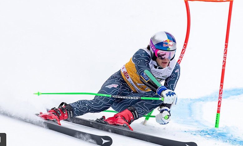 Red Bull alpine skier racing downhill on snowy slope during alpine skiing competition.