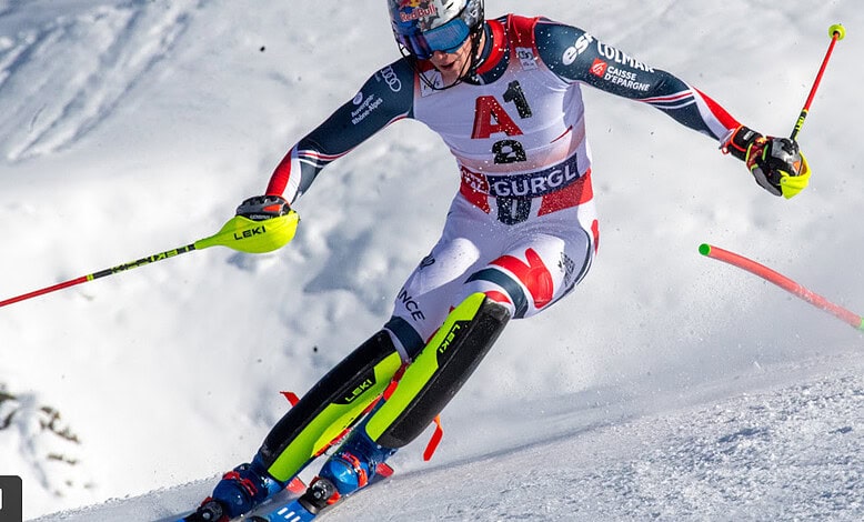 A skier racing down a snowy mountain slope, wearing a USA team outfit with red, white, and blue, using leki poles, showcasing winter sports and skiing expertise.