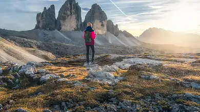 1. A hiker standing in a mountainous landscape during sunset, surrounded by rugged terrain and dramatic peaks, reflecting adventure and exploration for winter and outdoor enthusiasts.