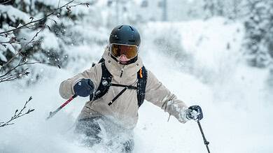 Skier wearing VALLON Crossroads™ goggles navigating fresh snow on a winter mountain slope.