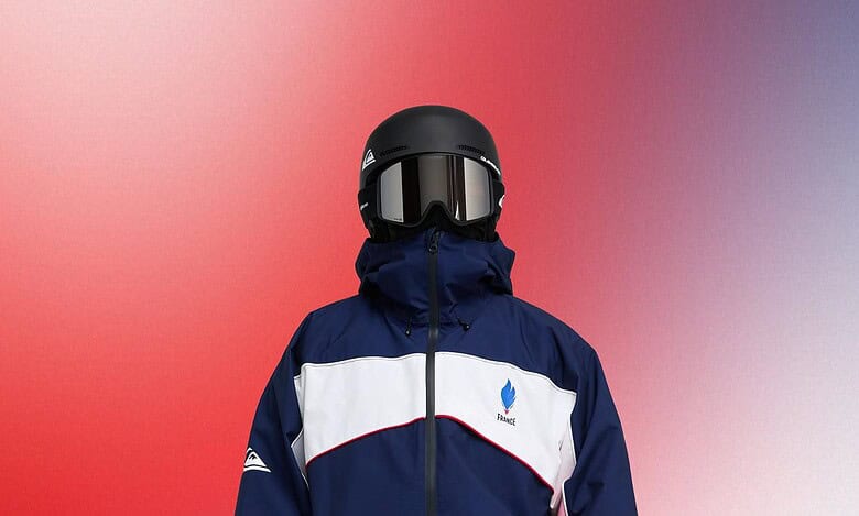 Child in winter snowboard gear including helmet, goggles, and insulated jacket and pants, standing against a colorful gradient background.