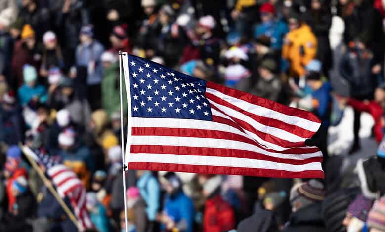 American flag waving at a crowded winter sports event with spectators in winter clothing.