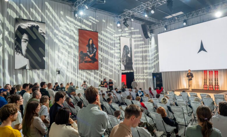 Large audience attending a conference with a speaker on stage and large screens in a modern event hall.