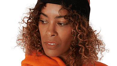 Woman wearing a black and orange knit beanie with a pom-pom and a bear mascot logo, paired with an orange hoodie.