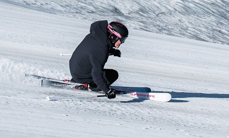 Skier in black winter gear carving through fresh snow on a clear day in the mountains.