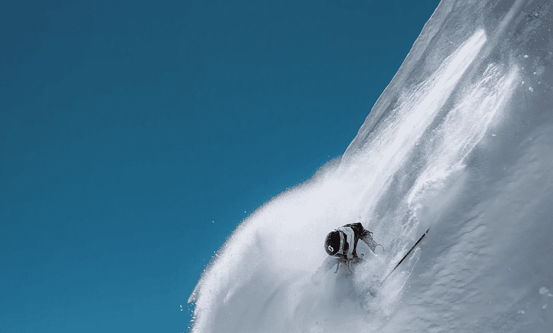 Skier descending a steep, snow-covered mountain slope during bright winter day, showcasing thrilling winter sports activity.