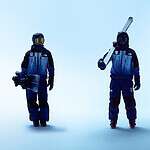 Two snowboarders in blue winter outfits standing on a pale blue background, one holding a snowboard and the other with a ski pole.