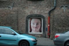 Großes Wandbild einer lachenden Frau in einer Fenstersituation auf einer Backsteinmauer.