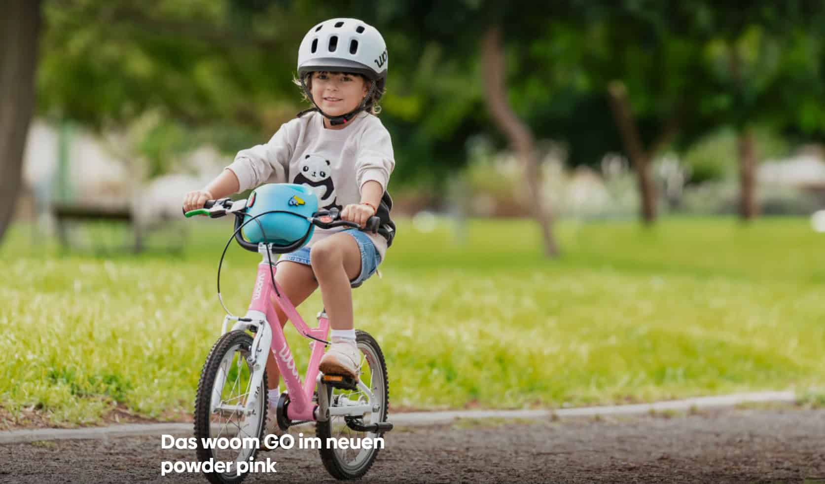 powder pink Junge Mädchen fährt Fahrrad im Park mit Helm und pinkem Fahrrad.