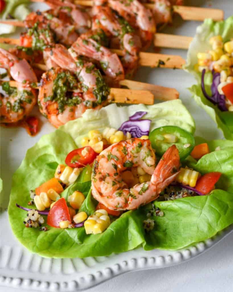 A close-up of a shrimp lettuce wrap with a corn salsa and shrimp skewers in the background.