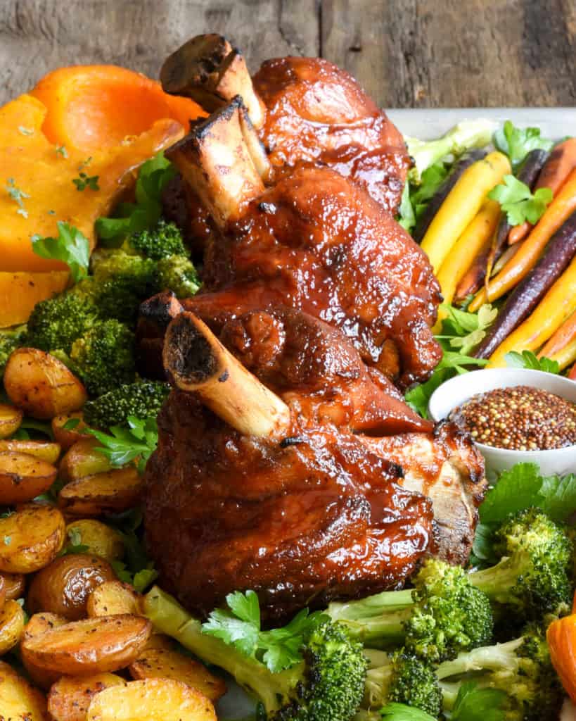 Three sticky BBQ pork hocks served with a variety of roasted vegges.