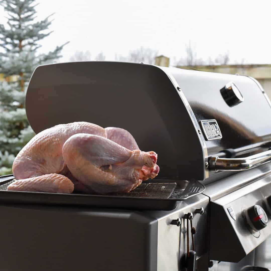 A trussed turkey on the side table of a grill in the winter.